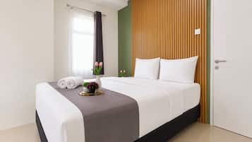 A neatly made bed with white linens, a grey throw, and a small vase with flowers.