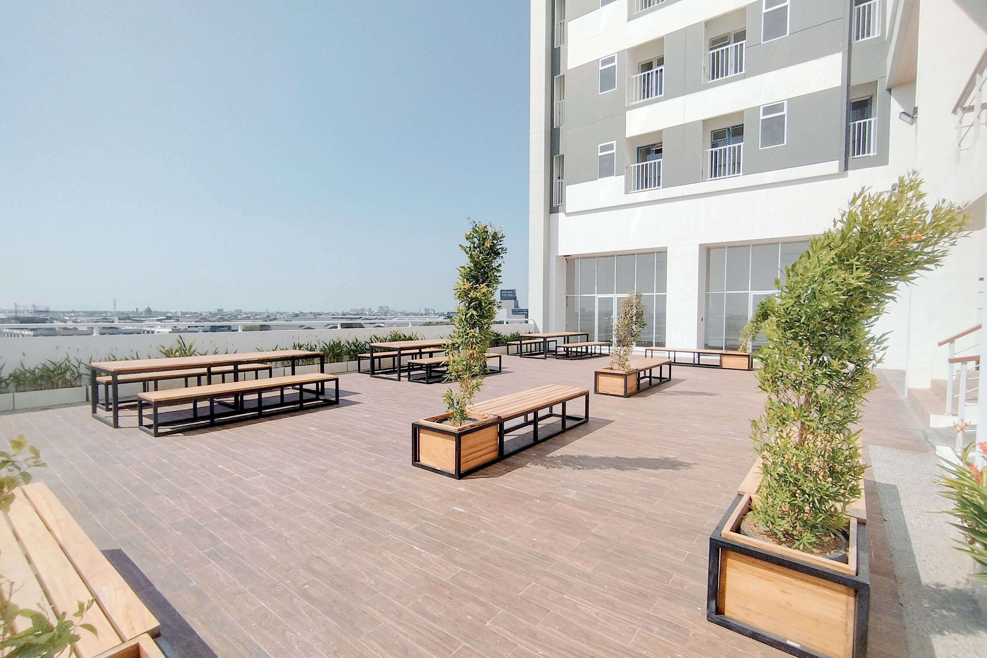 A rooftop terrace with wooden benches and planters, a modern building in the background, and a clear sky.