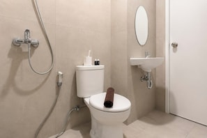 Et badeværelse med toilet, bidet, bruser, vask og spejl.