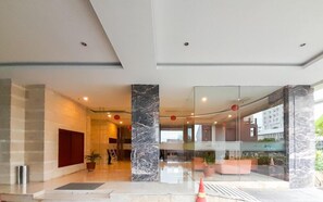 A modern hotel lobby with marble columns, a reception desk, and a glass partition. - Enjoyable Studio At Apartment Mataram City Palagan Yogyakarta (Ngaglik)