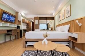 Quarto de hotel moderno com cama, mesas de cabeceira, escrivaninha e televisão.