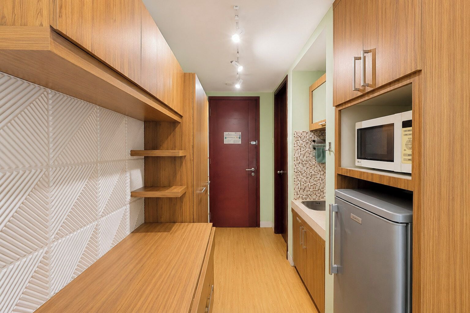 A narrow kitchen with wooden cabinets, a microwave, and a refrigerator.