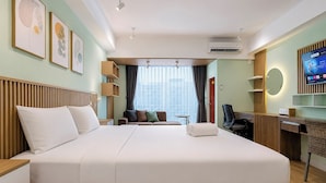 A hotel room with a large bed, a desk, a chair, a TV, and artwork on the wall. - Enjoyable Studio At Apartment Mataram City Palagan Yogyakarta (Ngaglik)