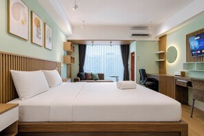 A hotel room with a large bed, a desk, a chair, a TV, and artwork on the wall. - Enjoyable Studio At Apartment Mataram City Palagan Yogyakarta (Ngaglik)