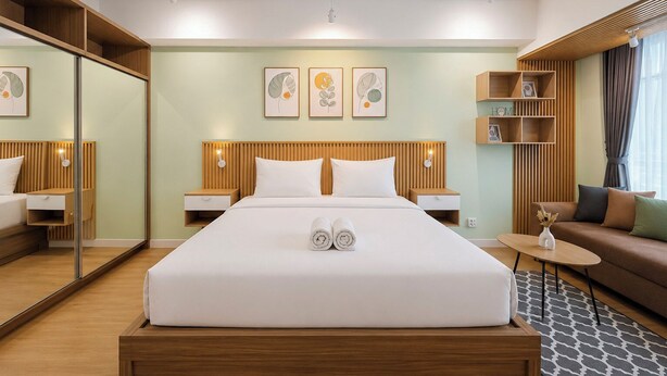 A hotel room with a large bed, bedside tables, a mirror, a sofa, and artwork on the walls. - Enjoyable Studio At Apartment Mataram City Palagan Yogyakarta (Ngaglik)