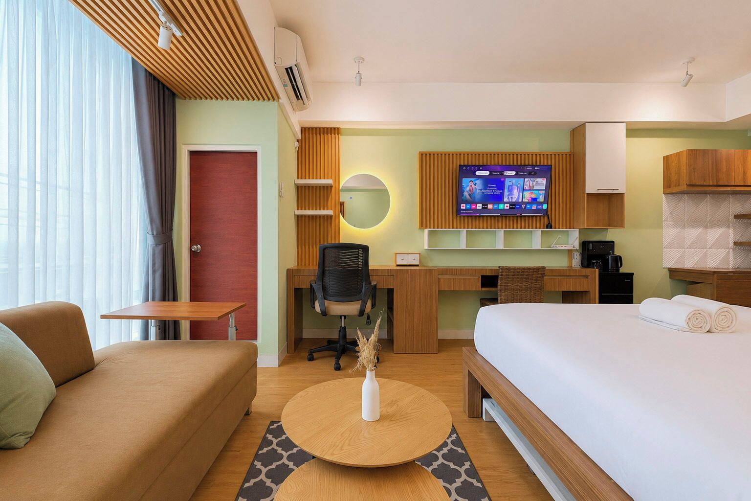 Habitación de hotel con cama, escritorio, silla, sofá, televisor y cafetera.