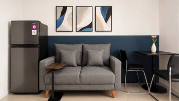 A modern kitchenette with a grey sofa, a black refrigerator, and abstract wall art.