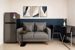 Eine moderne Küchenzeile mit einem grauen Sofa, einem schwarzen Kühlschrank und abstrakten Wandbildern.