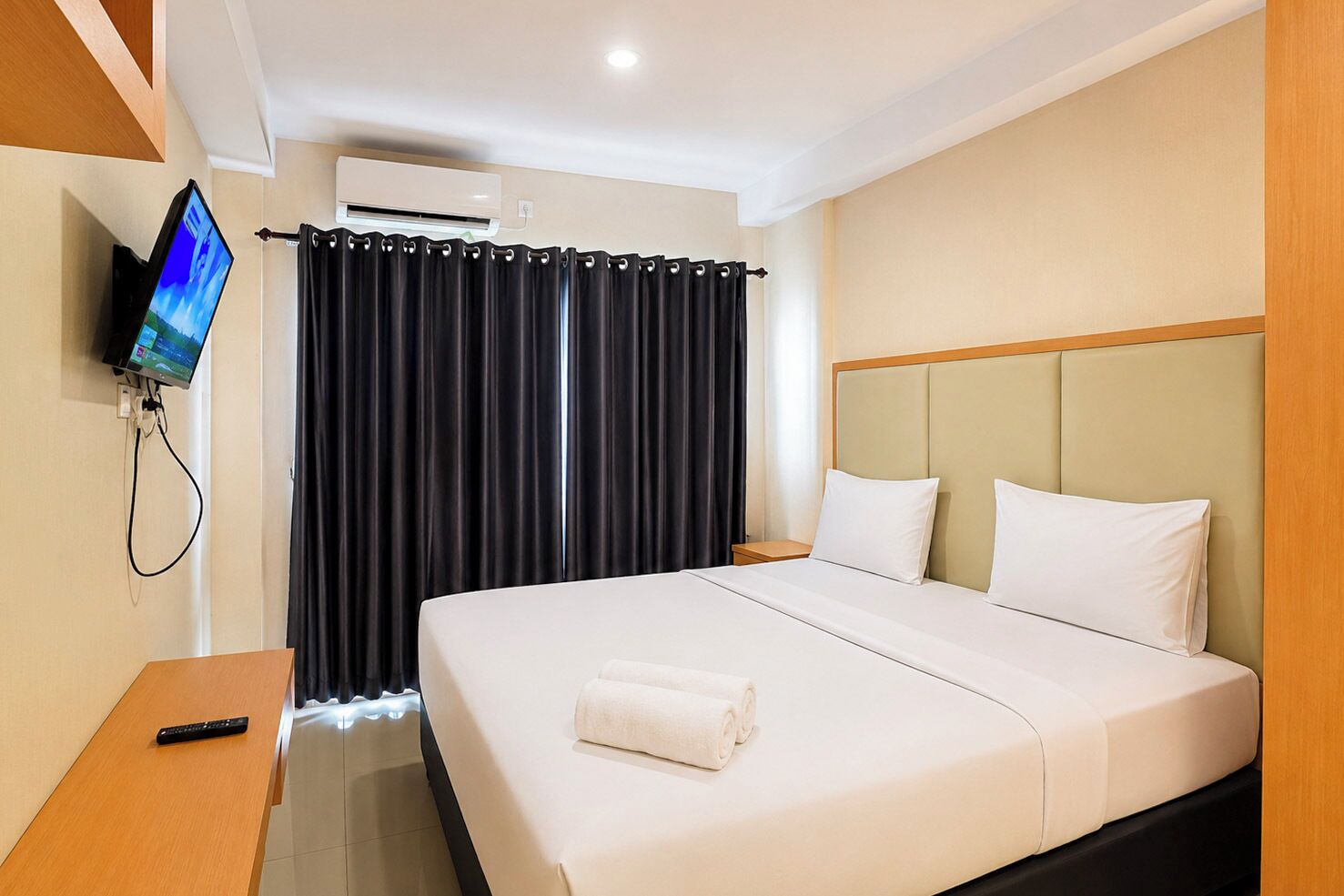 A hotel room with a bed, a TV mounted on the wall, an air conditioning unit, and a curtain.