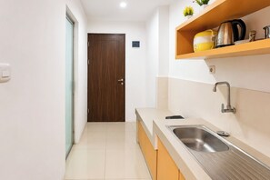 A modern kitchen with a stainless steel sink, wooden cabinets, and a wooden door. - Relaxing Studio At Apartment Skyview Medan (Medan)