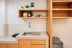 A compact kitchen with a sink, countertop, and wooden cabinets. There are potted plants on a shelf above the sink. - Relaxing Studio At Apartment Skyview Medan (Medan)