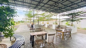 An outdoor cafe with tables and chairs, covered by a metal roof, surrounded by greenery. - Relaxing Studio At Apartment Skyview Medan (Medan)
