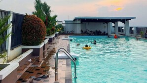 A swimming pool with a tiled deck and a covered area in the background. - Relaxing Studio At Apartment Skyview Medan (Medan)