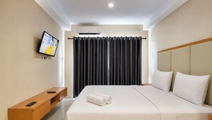 A hotel room with a bed, a TV mounted on the wall, a wooden bench, and a window with curtains. - Relaxing Studio At Apartment Skyview Medan (Medan)