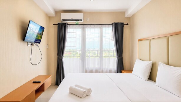 A hotel room with a bed, a TV mounted on the wall, a window with curtains, and a view of the outdoors. - Relaxing Studio At Apartment Skyview Medan (Medan)