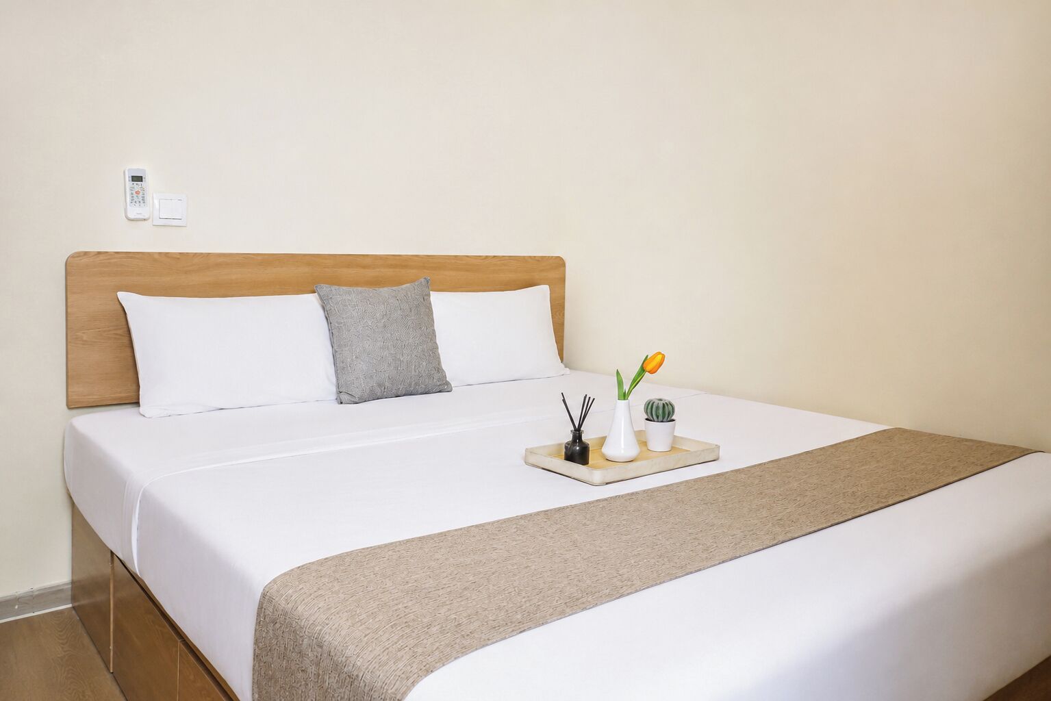 Una cama bien hecha con cabecera de madera, ropa de cama blanca y una bandeja con un florero y una planta pequeña.