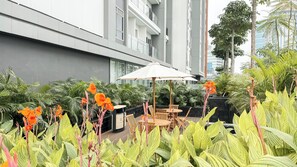 An outdoor seating area with tables and chairs, surrounded by lush greenery and flowering plants. - Elegant Studio At Apartment Antasari Place (Jakarta)