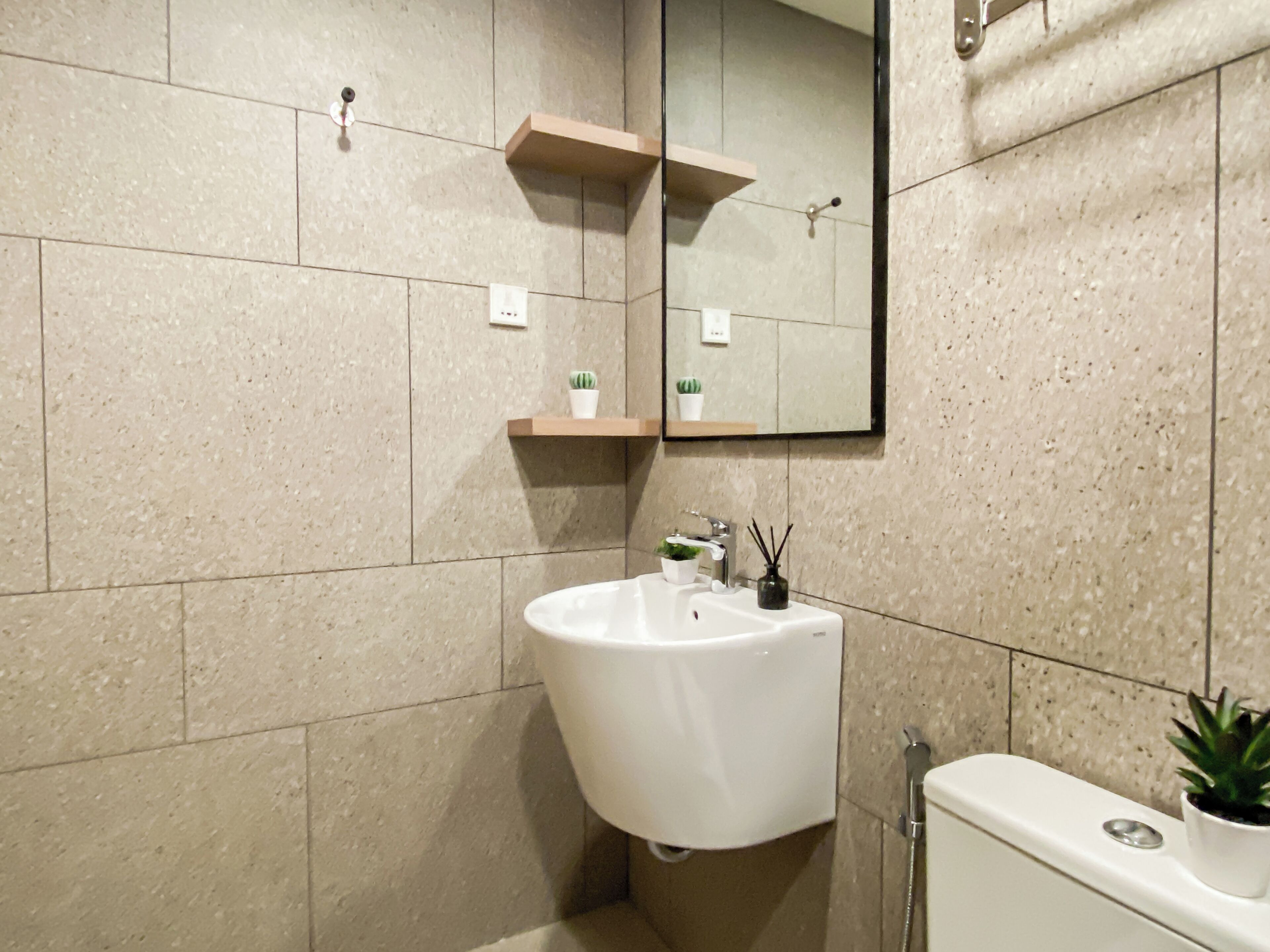 A modern bathroom with a white sink, a mirror, and a shower. There are two potted plants on the wall.