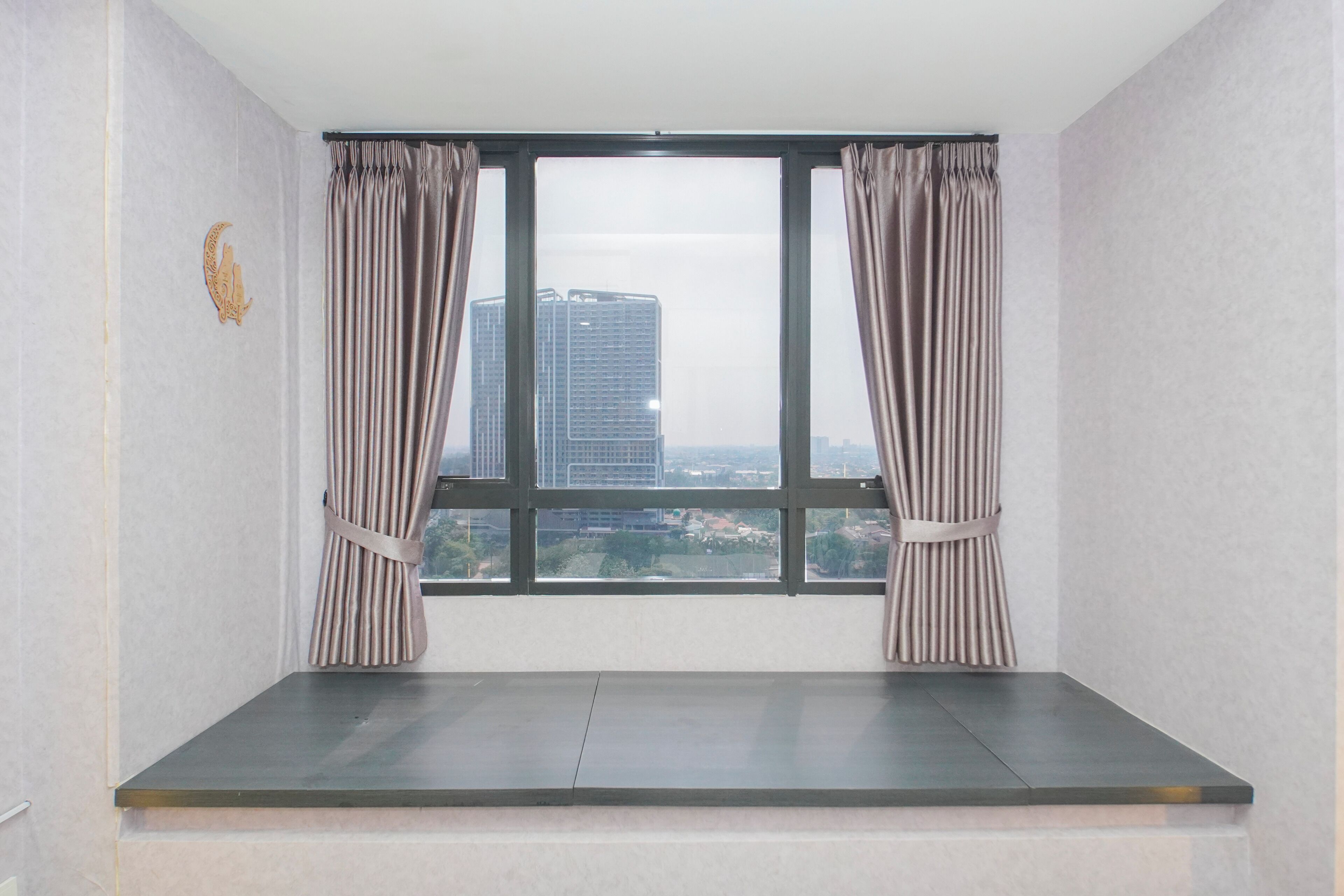 A room with a large window, curtains, and a view of buildings.
