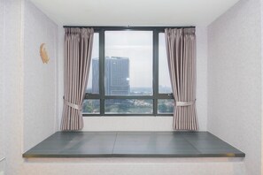 Ein Zimmer mit großem Fenster, Vorhängen und Blick auf Gebäude.
