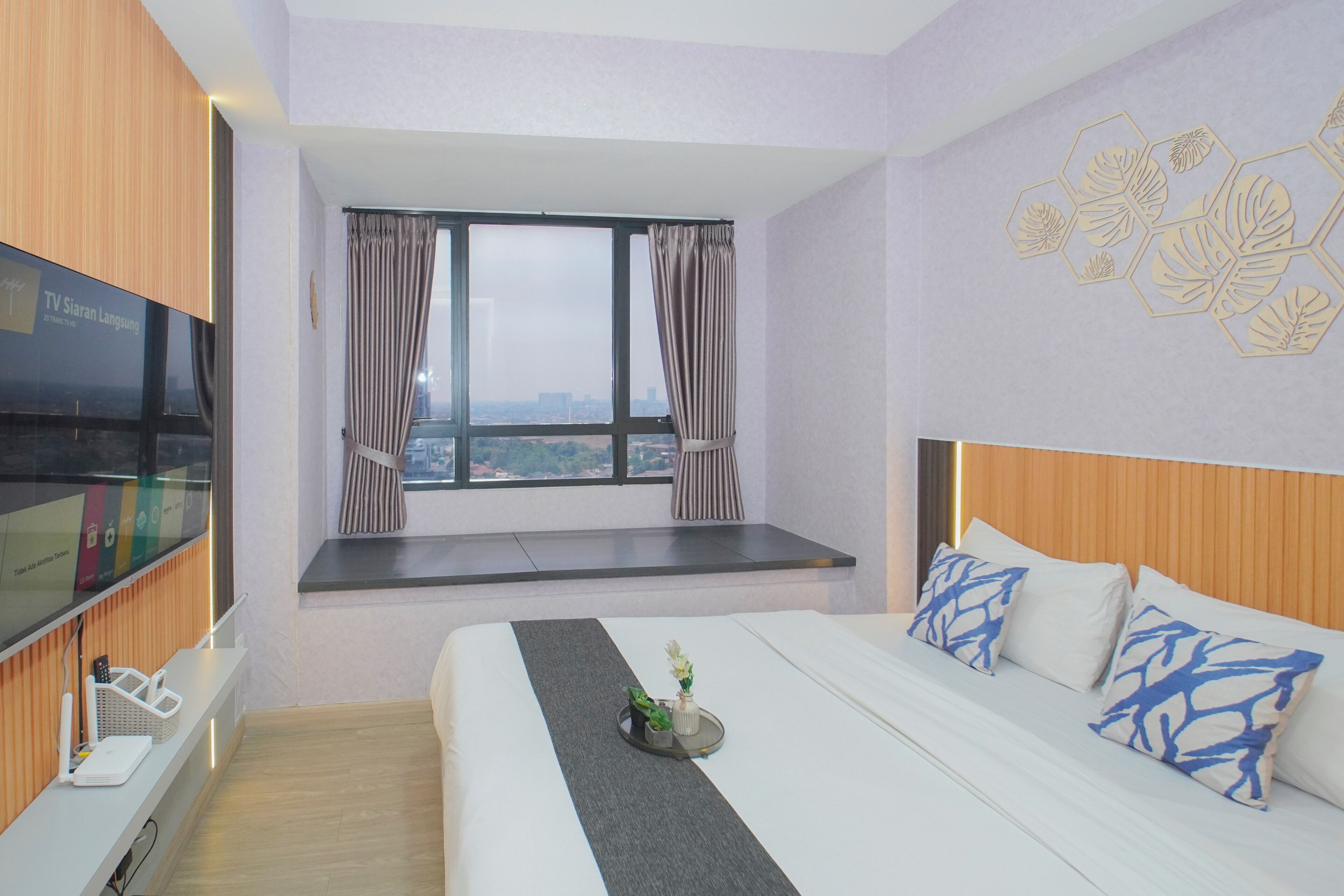 Ein Hotelzimmer mit Bett, Fernseher, Fenster mit Vorhängen und Blick auf die Stadt.