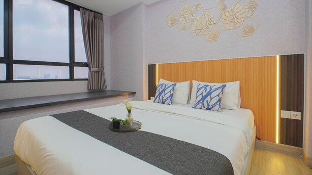 Ein Hotelzimmer mit einem großen Bett, Blick auf die Stadt durch ein Fenster und einer dekorativen Wandverkleidung.