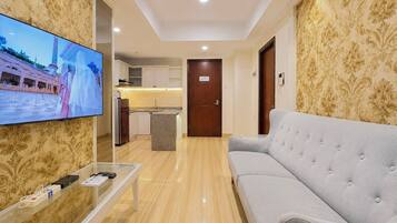 Habitación de hotel con televisión, sofá, mesa de centro y zona de cocina al fondo.