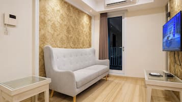 A modern living room with a grey sofa, a glass coffee table, a flat-screen TV, and an air conditioning unit.