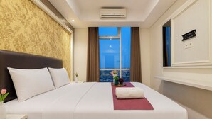 Ein Hotelzimmer mit einem großen Bett, einem Nachttisch, einer Vase mit Blumen, einem Fenster mit Blick auf die Stadt und einer Klimaanlage.