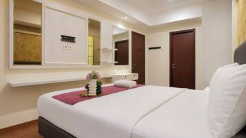 A hotel room with a bed, a vanity with a mirror, a small plant, and a wall-mounted control panel.