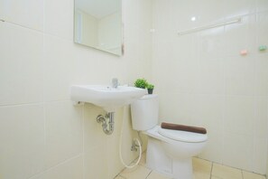 Casa de banho com lavatório branco, sanita e espelho sobre o lavatório.