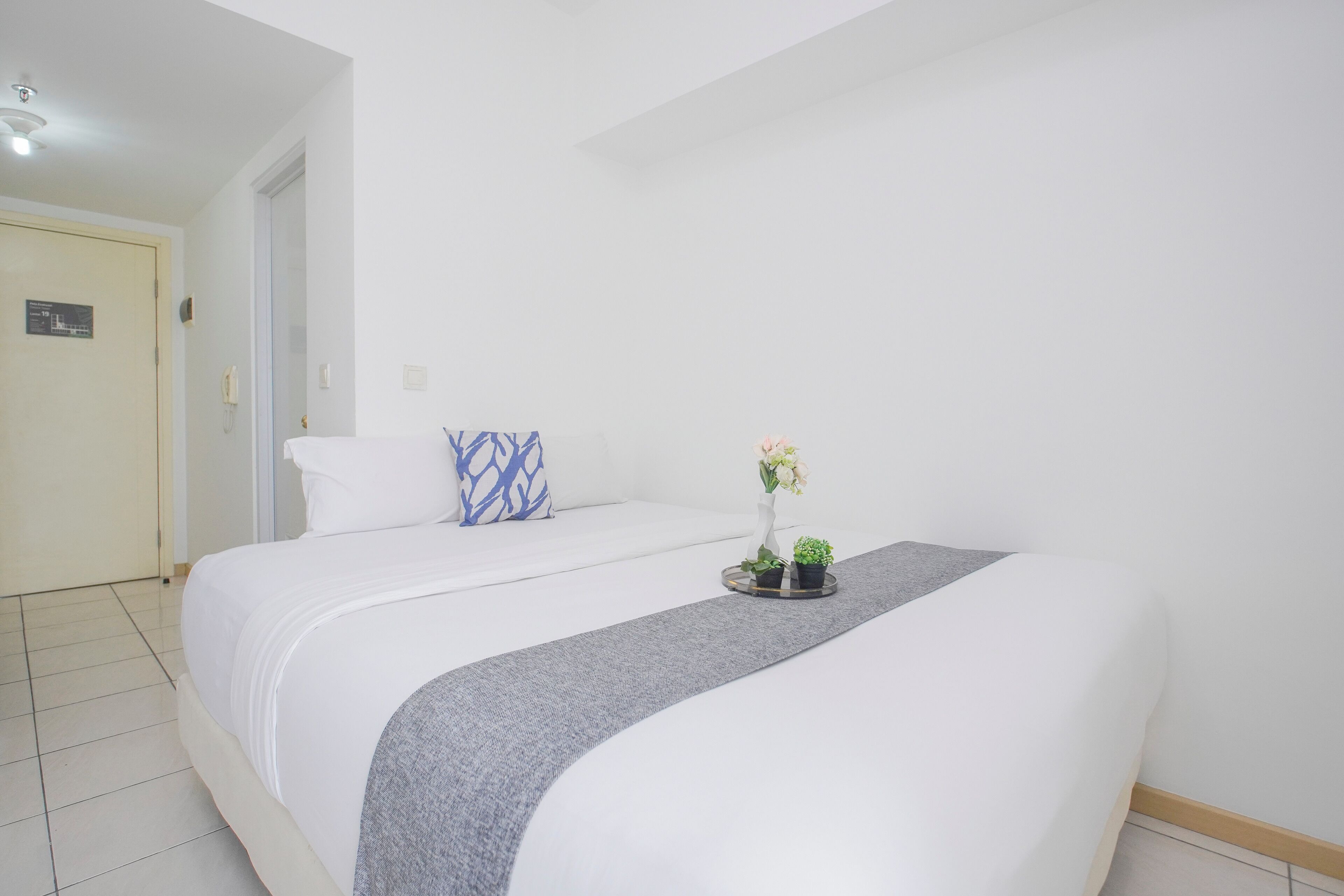 Ein Hotelzimmer mit einem Bett, einem Nachttisch mit Blumen und einer Tür mit einem Schild.