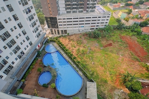 A rooftop swimming pool with a checkered pattern, surrounded by greenery and adjacent to a multi-story building. - Elegant Cozy Living Studio At Apartment Parkland Avenue (Tangerang)