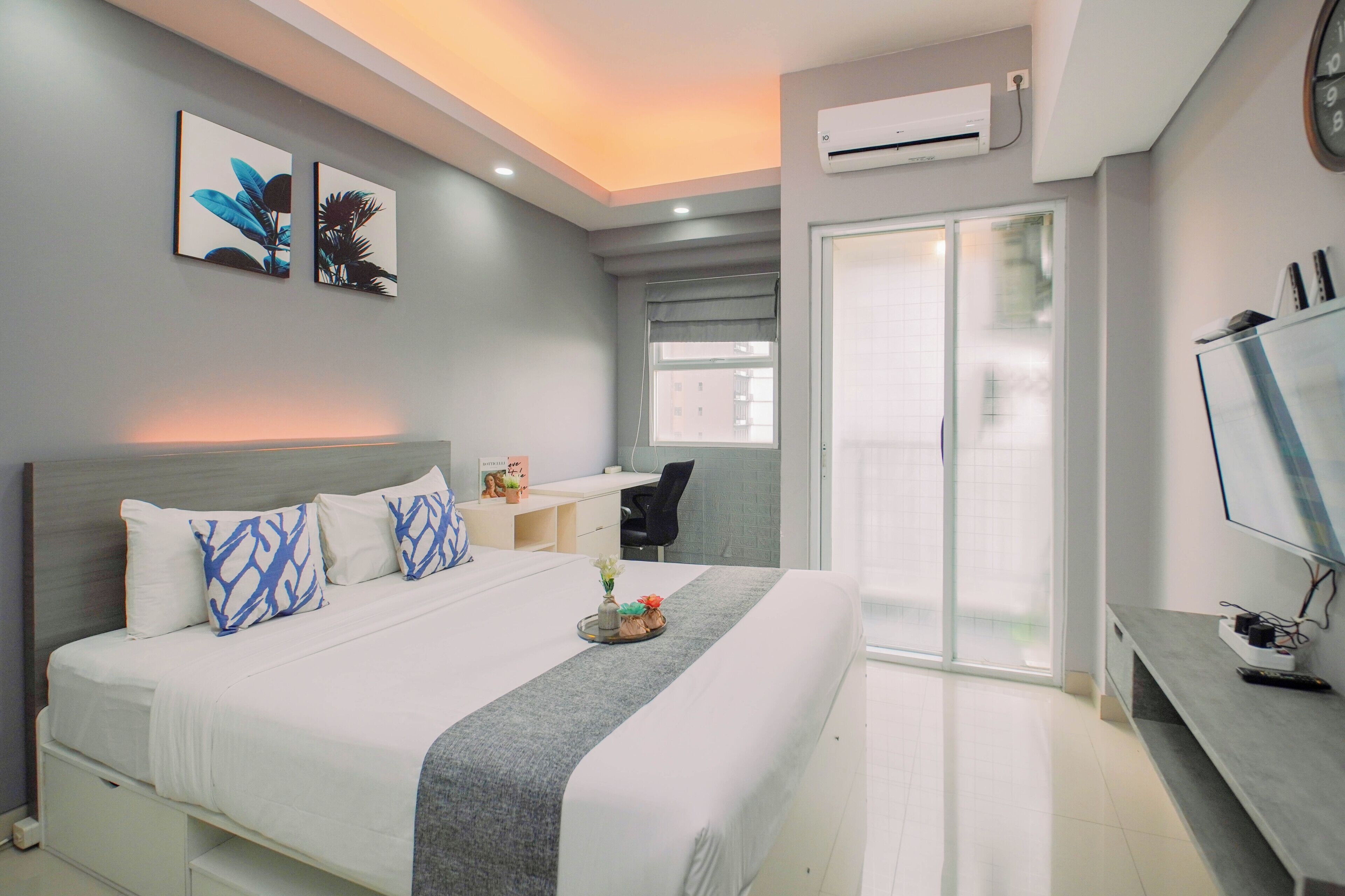 A modern hotel room with a large bed, a desk, a TV, and a sliding glass door to the balcony.