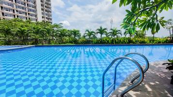A swimming pool with a checkered pattern, surrounded by greenery and a tall building in the background.