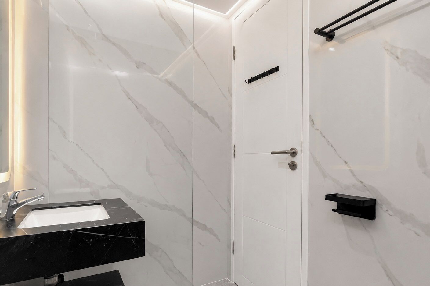 A bathroom with a marble wall, a black sink, and a shower area.