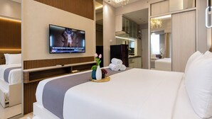 Una moderna camera d'albergo con un grande letto, una TV a schermo piatto fissata alla parete, un tavolino con un vaso e degli asciugamani, e un bagno separato.