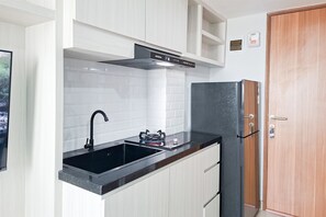 A compact kitchen with white cabinetry, a black countertop, a stainless steel sink, and a black refrigerator. - Nice And Tidy Studio Room At Apartment Cisauk Point (Cisauk)