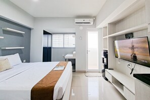 A modern hotel room with a bed, a flat-screen TV, a desk, and a window with blinds. - Nice And Tidy Studio Room At Apartment Cisauk Point (Cisauk)
