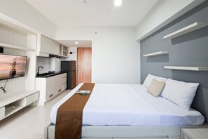 A modern hotel room with a bed, a TV, a kitchenette, and a bathroom. - Nice And Tidy Studio Room At Apartment Cisauk Point (Cisauk)