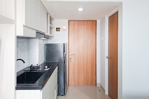 A compact kitchen with white cabinets, a black countertop, a built-in stove, and a refrigerator. - Nice And Tidy Studio Room At Apartment Cisauk Point (Cisauk)