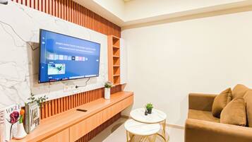 A modern living room with a flat-screen TV mounted on a marble wall, a wooden console table with a smartphone and decorative items, a round white table with gold legs, and a brown sofa.