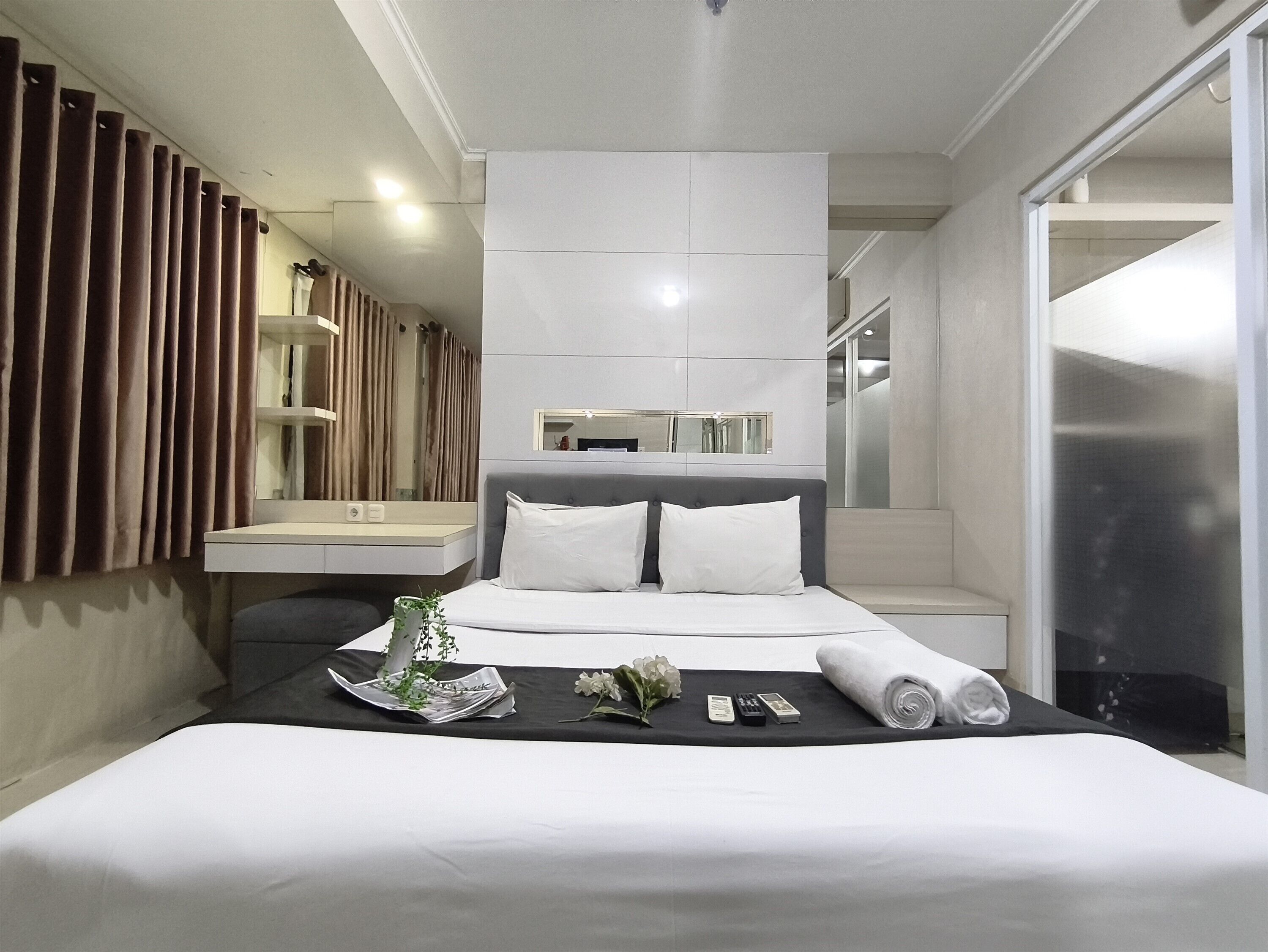 A hotel room with a large bed, a bedside table, a mirror, and a view of the bathroom.