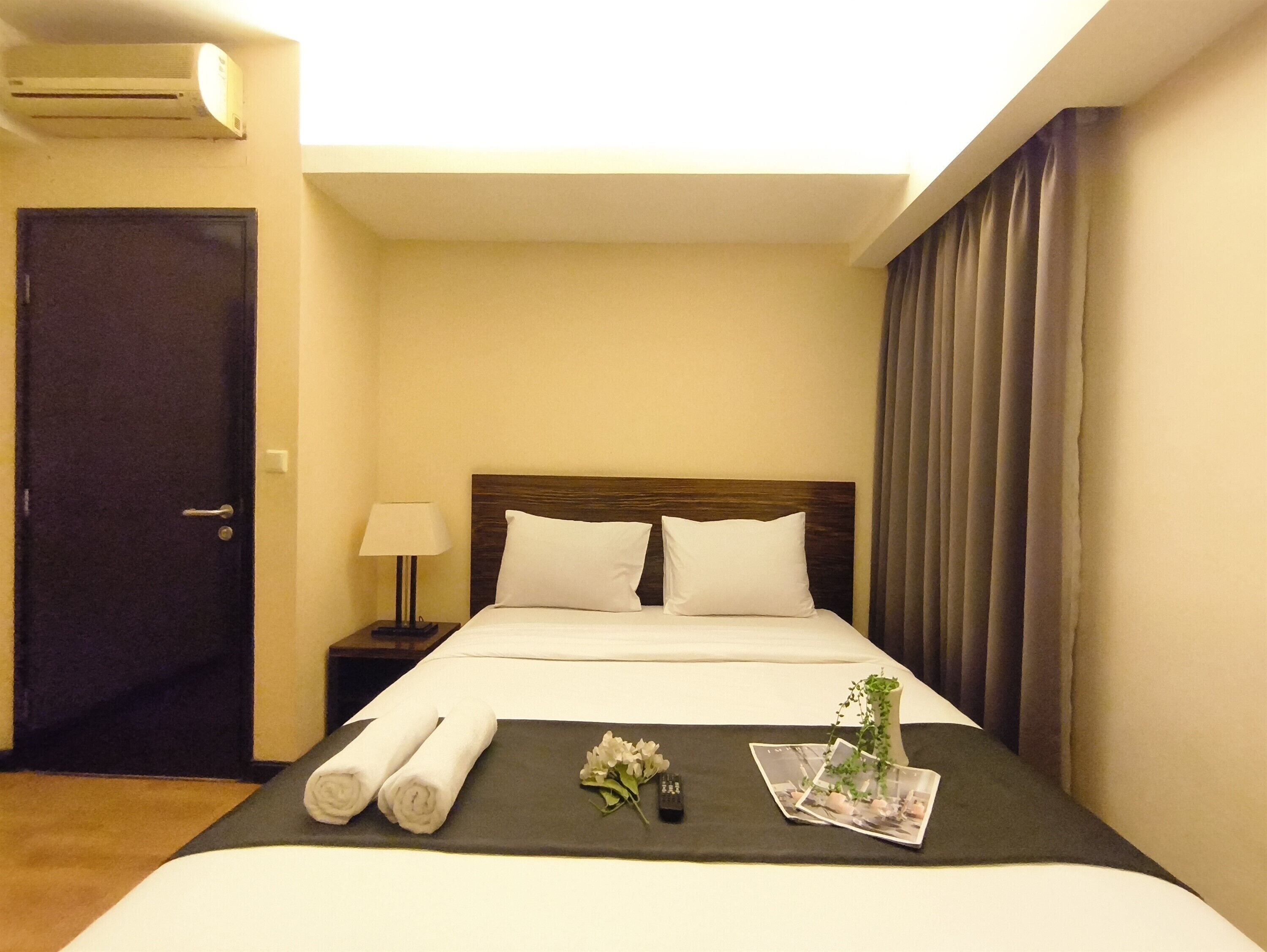 Habitación de hotel con una cama, una mesita de noche, una lámpara, una puerta y una ventana con cortinas.