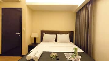 A hotel room with a bed, a nightstand, a lamp, a door, and a window with curtains.