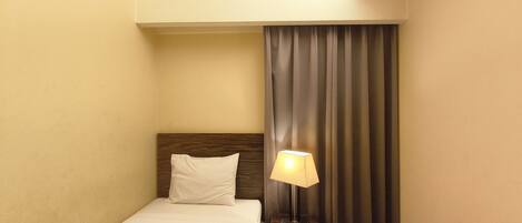 A hotel room with a bed, a nightstand, a lamp, and a window with curtains.