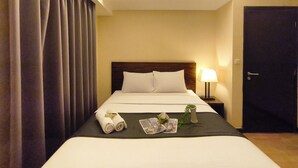 A hotel room with a bed, a nightstand, a lamp, a door, and a window with curtains. - Best Deal 3Br Apartment Braga City Walk (Bandung)