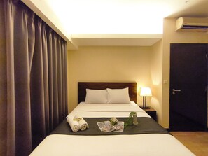 A hotel room with a bed, a nightstand, a lamp, a door, and a window with curtains. - Best Deal 3Br Apartment Braga City Walk (Bandung)