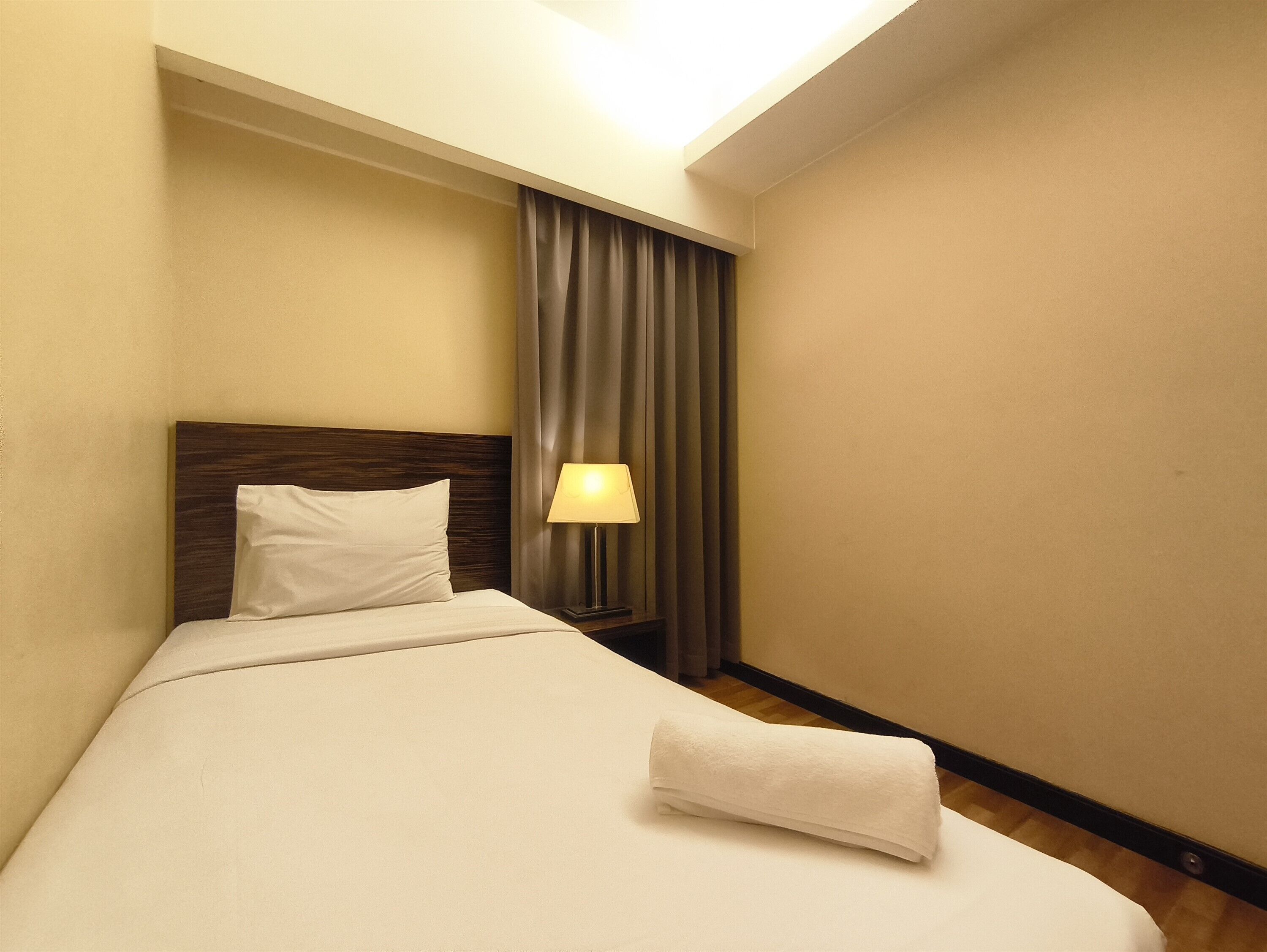 Ein Hotelzimmer mit einem Einzelbett, einem Nachttisch mit Lampe und einem Fenster mit Vorhängen.