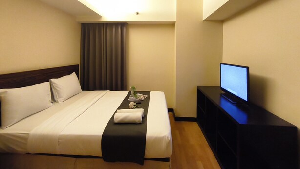 A hotel room with a bed, a flat-screen TV, and a small table with a remote control. - Best Deal 3Br Apartment Braga City Walk (Bandung)